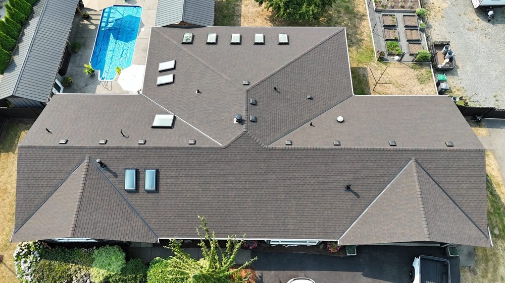 Large asphalt shingle roof over a full property, overhead drone view